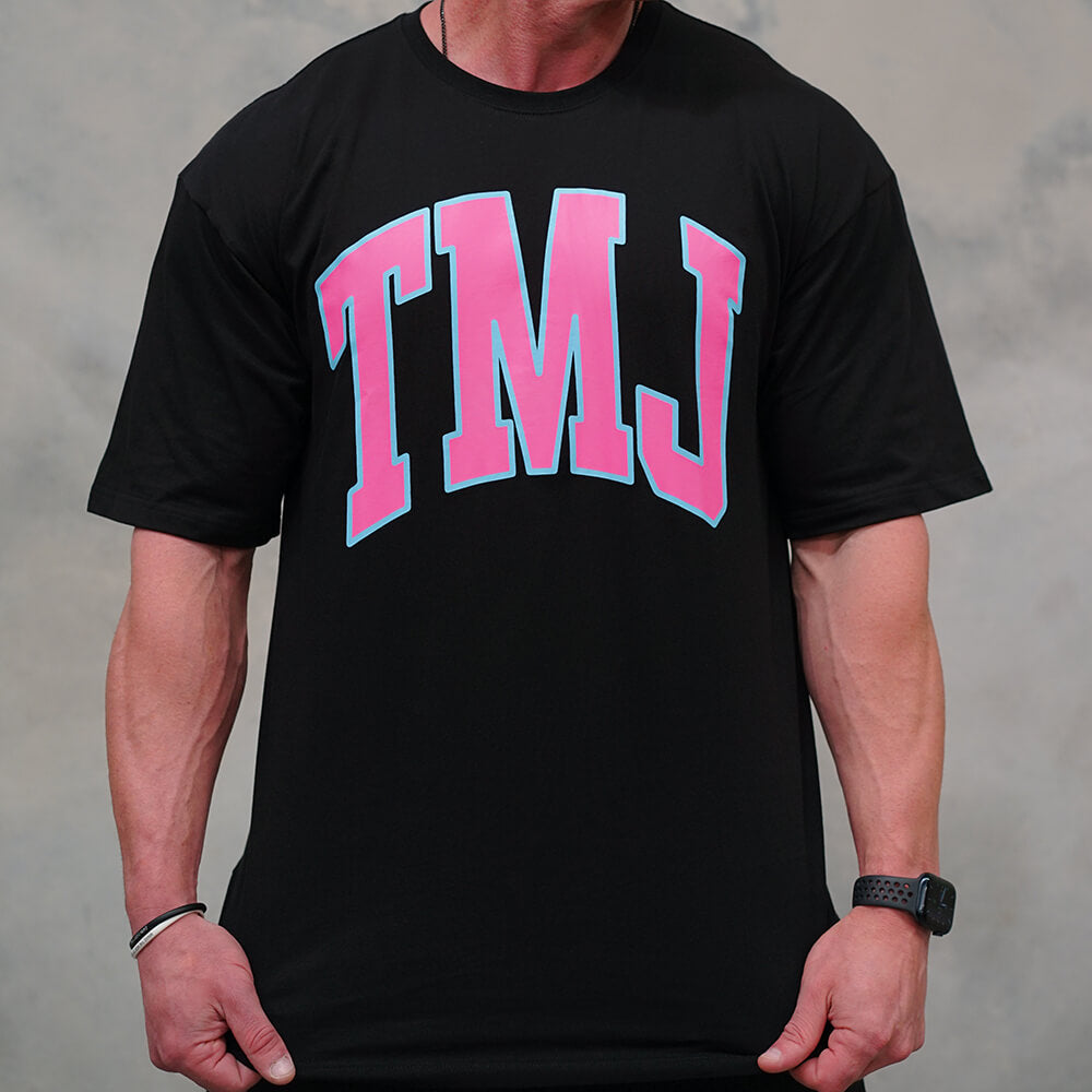 Male wearing black oversized t-shirt with large pink "TMJ" logo with light blue outline representing Miami Vice colours.