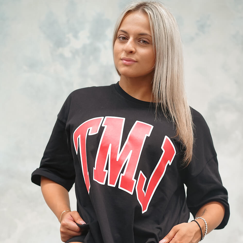 Female wearing black oversized warm-up tee with large red 'TMJ' print on the front