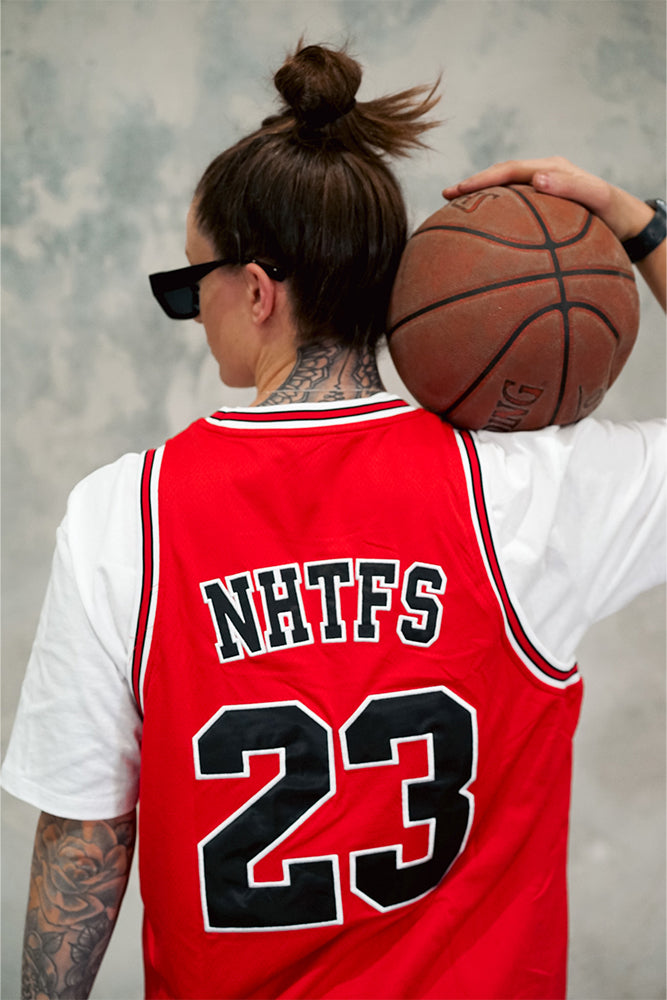 Female wearing Chicago Bulls inspired limited edition red TMJ Apparel 2023 Basketball Jersey showing the back with the player name &quot;NHTFS&quot; and number &quot;23&quot; below it in black.
