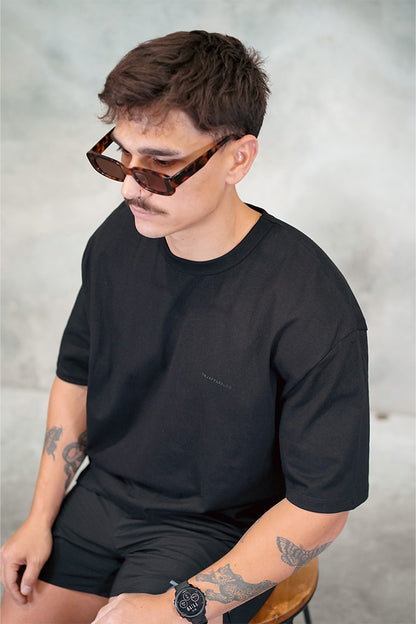 Male wearing TMJ Apparel 1993 in the colour Black showing the minimal design with a small 3D “TMJAPPARELCO” on front left chest.
