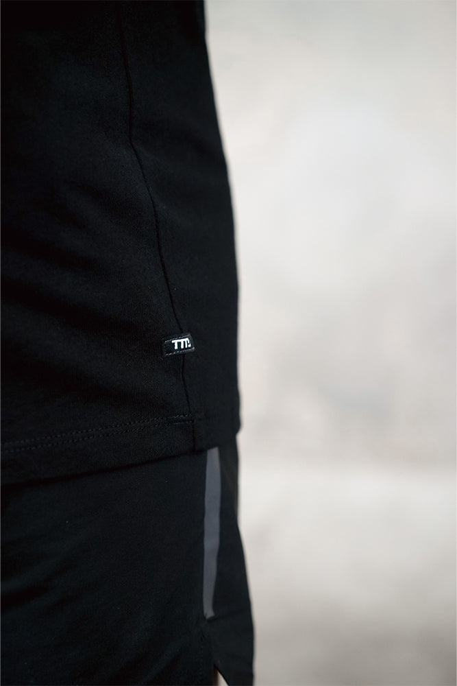 Close up of TMJ Apparel 1993 Tee in Black showing the small TMJ label on left hip side seam.