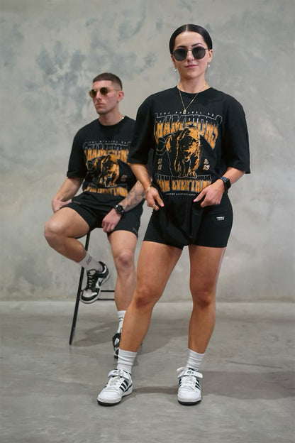Male &amp; Female wearing TMJ Apparel 1993 Champions Tee in Gold with a large print on the front with the words “TMJ Apparel Co”, “Champions” “Earn Everything” &amp; Premium Athleticulture Goods”.