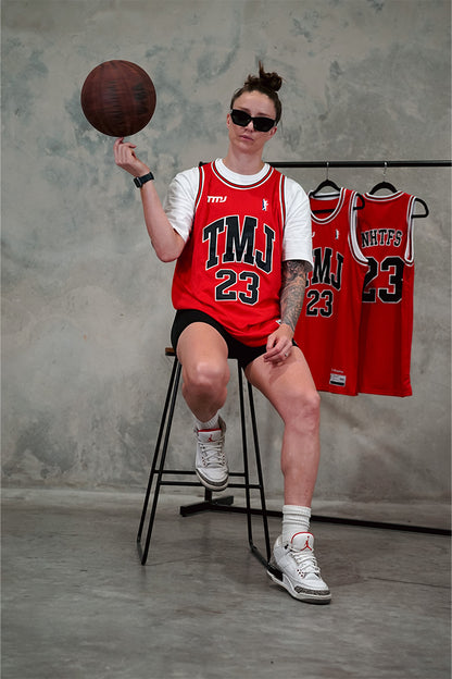 Female wearing Chicago Bulls inspired limited edition red TMJ Apparel 2023 Basketball Jersey showing &quot;TMJ&quot; with the number &quot;23&quot; in black on the front.