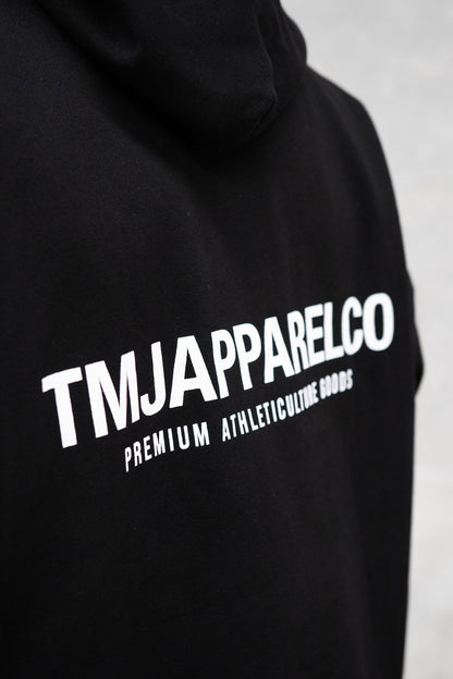 Close up of TMJ Apparel Athleticulture Hoodie in Black showing the back of the hoodie with white text saying TMJAPPARELCO Premium Athleticulture Goods in the middle centre of back.