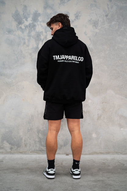  Male wearing TMJ Apparel Athleticulture Hoodie in Black showing the back of the hoodie with white text saying TMJAPPARELCO Premium Athleticulture Goods in the middle centre of back.