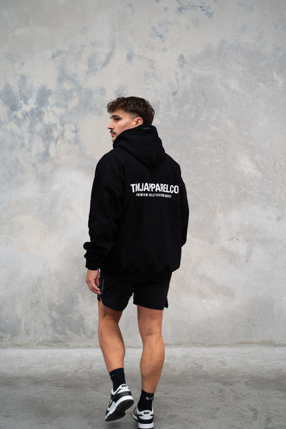  Male wearing TMJ Apparel Athleticulture Hoodie in Black showing the back of the hoodie with white text saying TMJAPPARELCO Premium Athleticulture Goods in the middle centre of back.