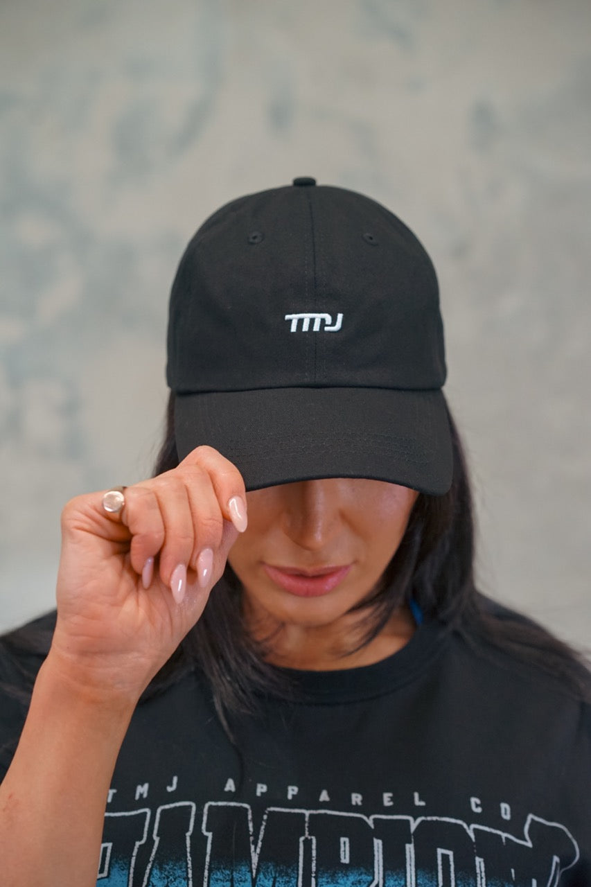 Female wearing black Chino Cap showing the minimal design with small &quot;TMJ&quot; logo on front of cap.