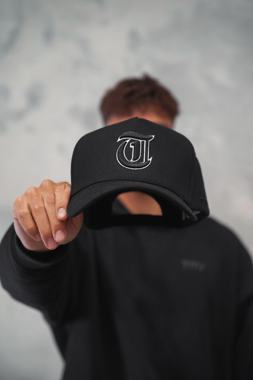 Male holding Black TMJ Apparel 9PHIFTY A-Frame Snapback Hat with Black 3D Embroidered Magna Carta T Logo with white outline on the front.