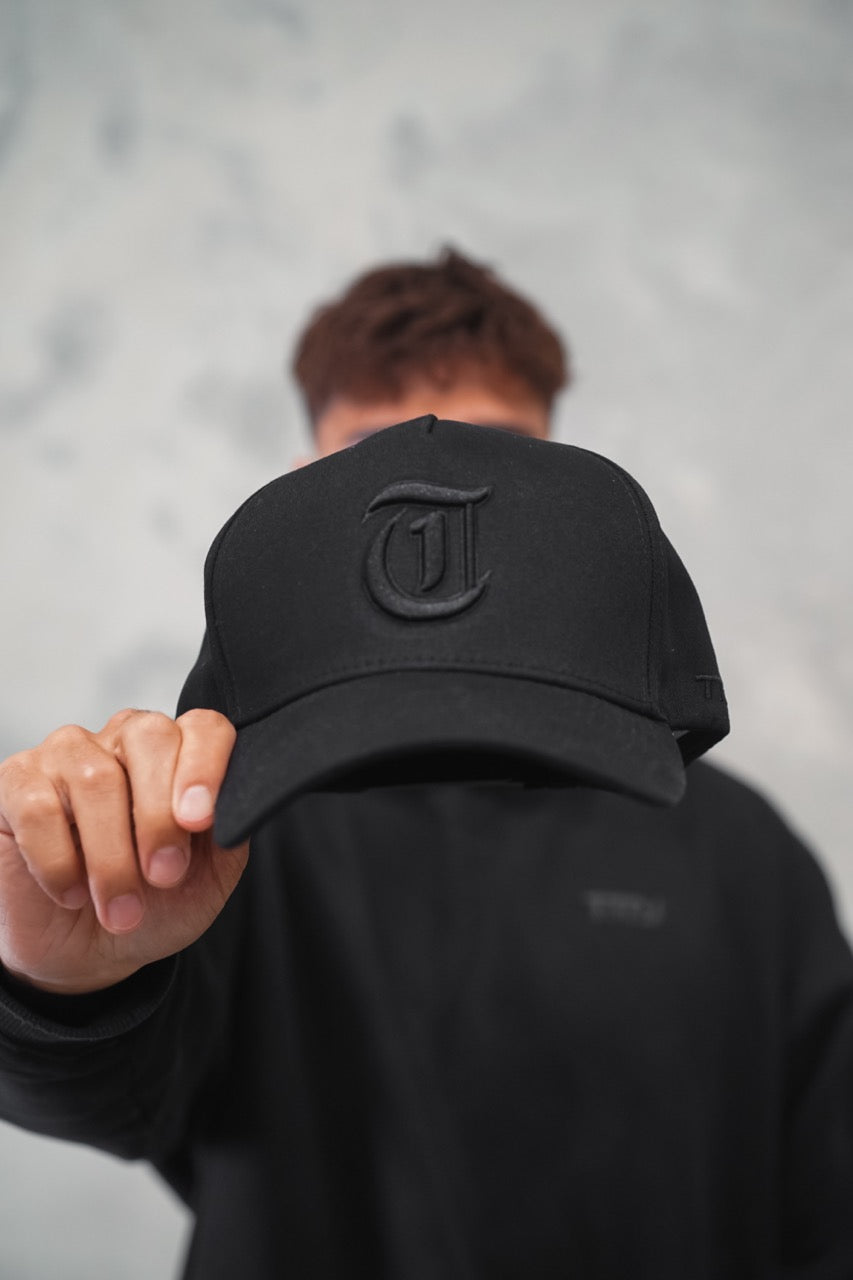 Male holding Black TMJ Apparel 9PHIFTY A-Frame Snapback Hat with Black 3D Embroidered Magna Carta T Logo with black outline on the front.