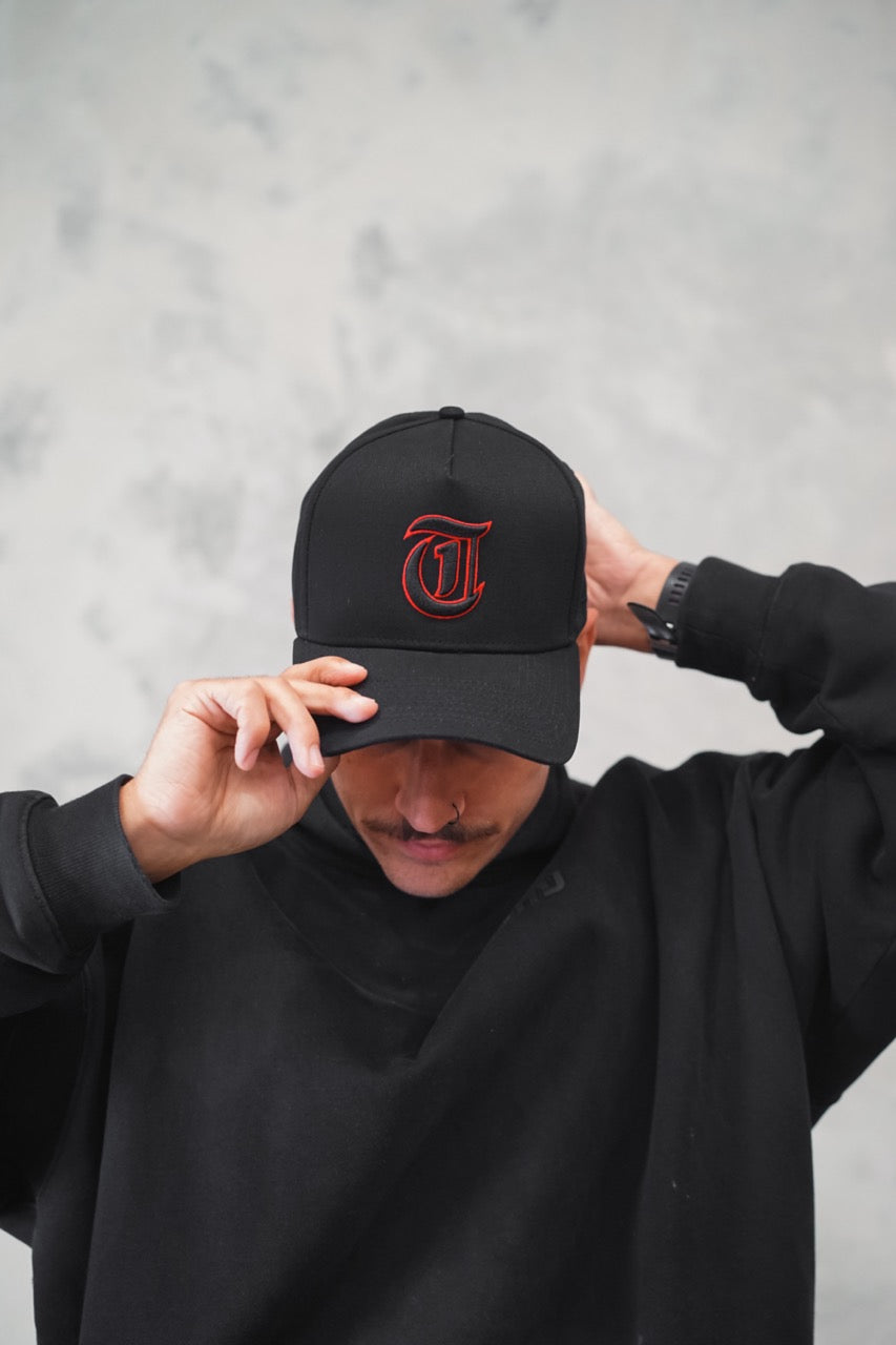 Male putting on Black TMJ Apparel 9PHIFTY A-Frame Snapback Hat with Black 3D Embroidered Magna Carta T Logo with red outline on the front.