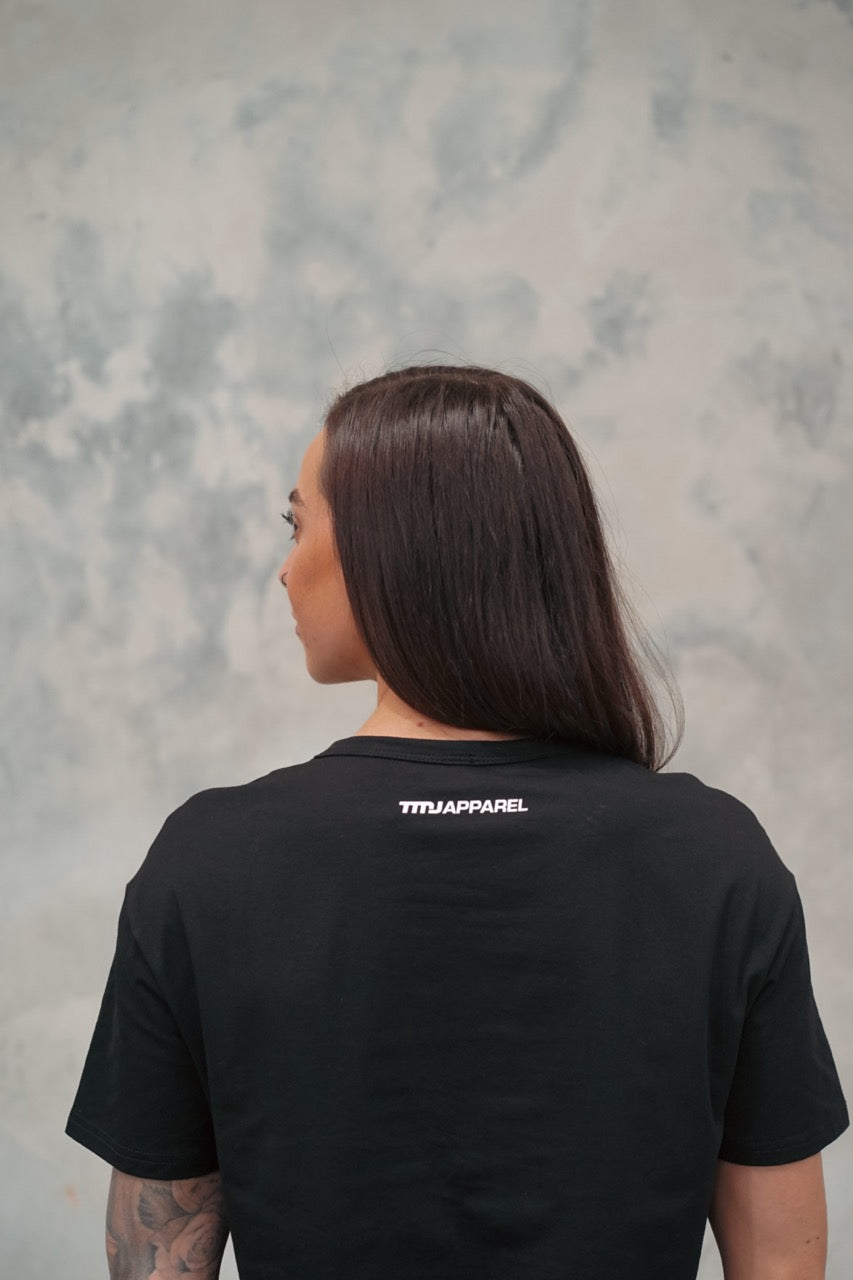 Female wearing TMJ Apparel Cropped Tee in Black showing the small white “TMJApparel” logo on nape of neck.