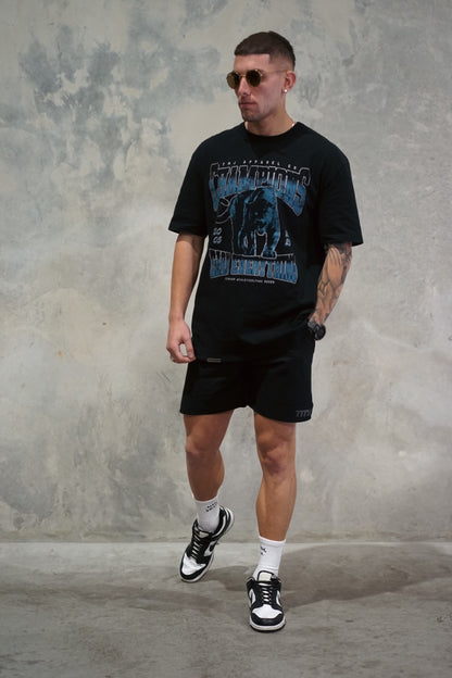 Male wearing TMJ Apparel 1993 Champions Tee in Blue with a large print on the front with the words “TMJ Apparel Co”, “Champions” “Earn Everything” &amp; Premium Athleticulture Goods”.