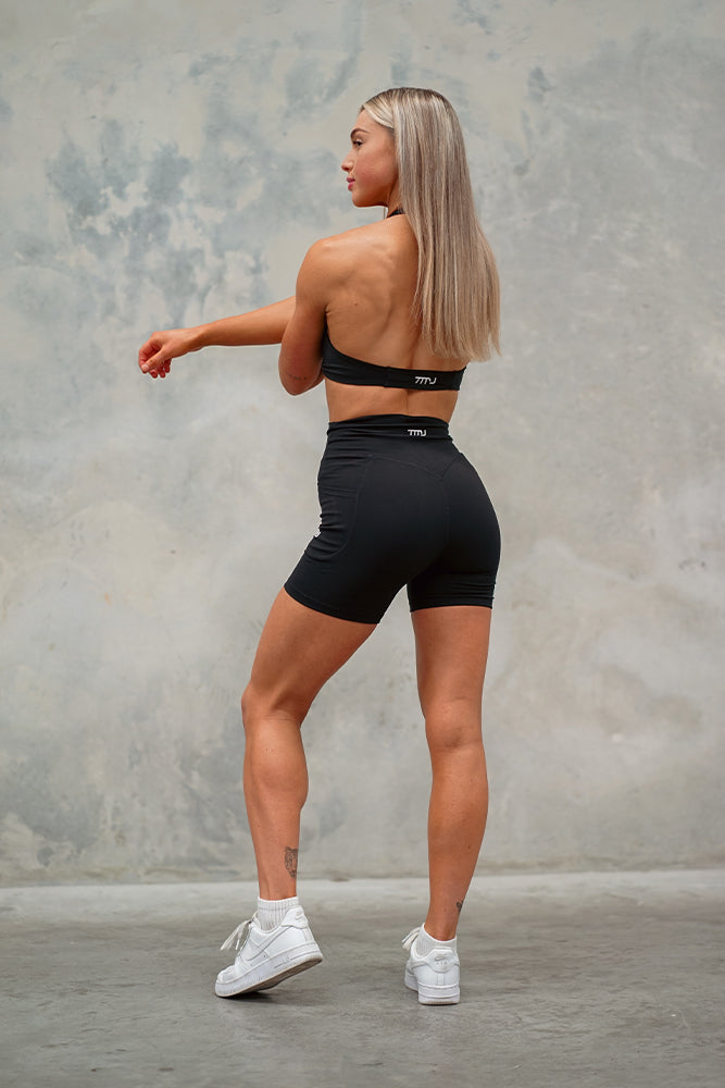 Female wearing Amy Twist Front Bra and Gigi Shorts in Black showing the halter-neck open back design of the bra and squat-proof design of the shorts.