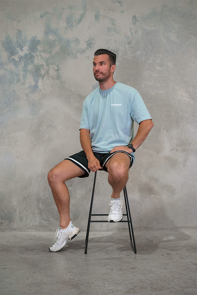 Male wearing TMJ Apparel Athleticulture Tee in Powder Blue front of the shirt with white text saying TMJAPPARELCO Premium Athleticulture Goods on left of chest