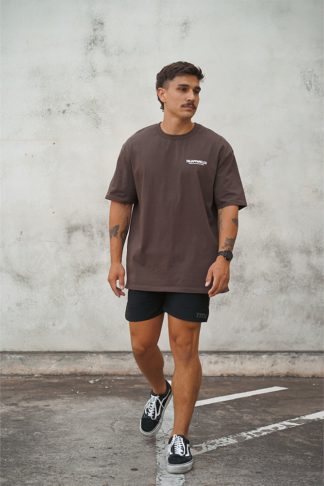 Male wearing TMJ Apparel Athleticulture Tee in Brown front of the shirt with white text saying TMJAPPARELCO Premium Athleticulture Goods on left of chest