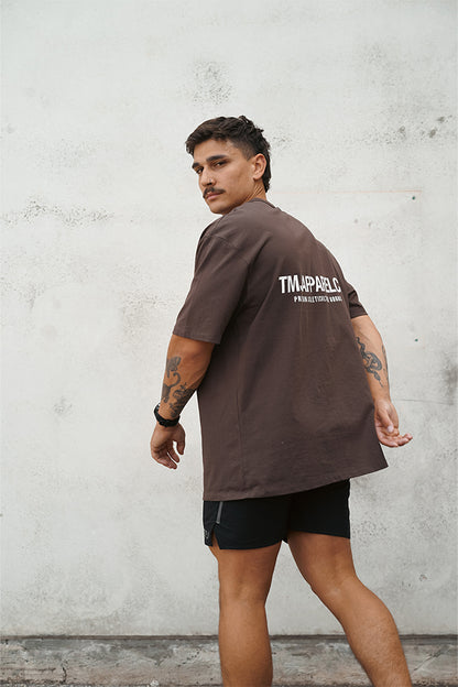 Male wearing TMJ Apparel Athleticulture Tee in Brown showing the back of the shirt with white text saying TMJAPPARELCO Premium Athleticulture Goods in the the middle centre of back