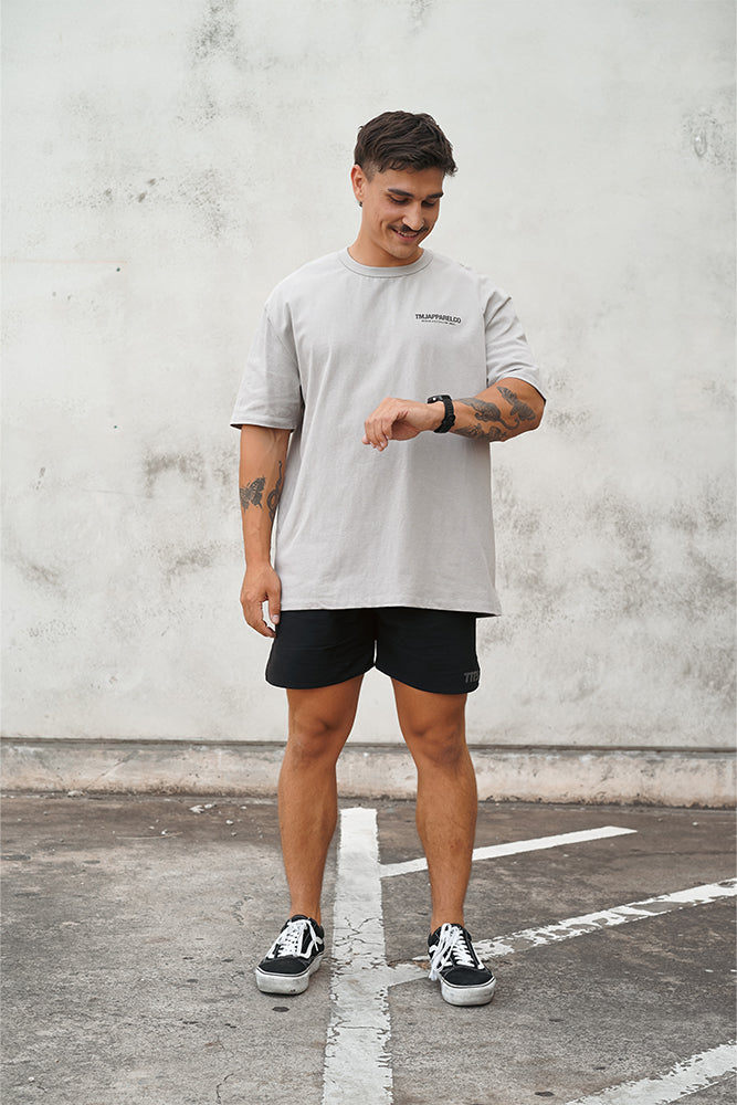 Male wearing TMJ Apparel Athleticulture Tee in Dune front of the shirt with white text saying TMJAPPARELCO Premium Athleticulture Goods on left of chest