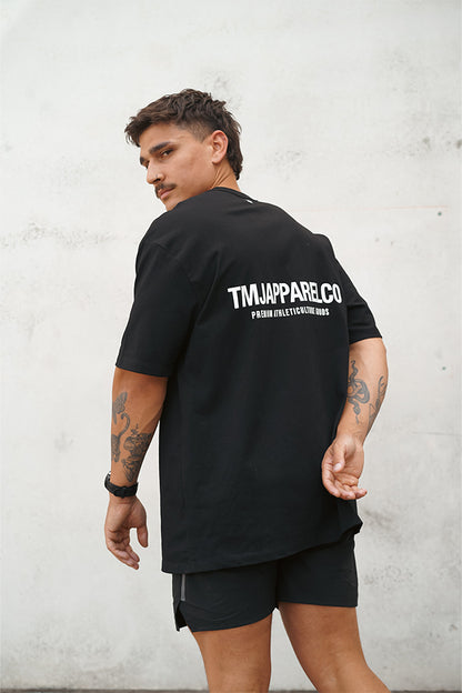 Male wearing TMJ Apparel Athleticulture Tee in Black showing the back of the shirt with white text saying TMJAPPARELCO Premium Athleticulture Goods in the the middle centre of back